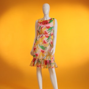 Puede incluir: Un vestido sin mangas con estampado floral en tonos amarillos, rosas, rojos y verdes. El vestido tiene un dobladillo con volantes y un corpiño ajustado.