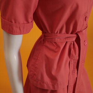 May include: A coral red short-sleeved dress with a button-up front and a matching belt. The dress has a skirt with a slight A-line shape.