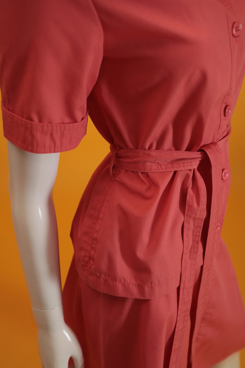 May include: A coral red short-sleeved dress with a button-up front and a matching belt. The dress has a skirt with a slight A-line shape.