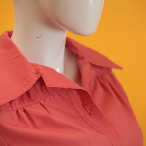 May include: Close-up of a coral pink button-down shirt with a pointed collar. The shirt is made of a soft, smooth fabric.