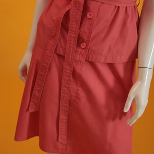 May include: A coral pink short-sleeved dress with a matching belt. The dress has a button-up front and a skirt with a slight A-line shape.