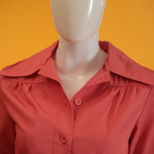 May include: A coral pink button-down shirt with a collar and short sleeves.