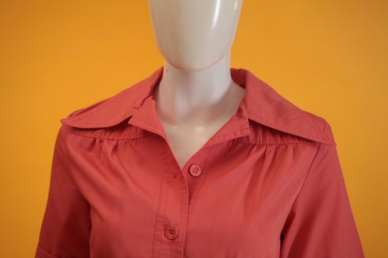 May include: A coral pink button-down shirt with a collar and short sleeves.