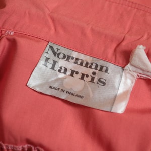 May include: A white label with black text that reads "Norman Harris" and "Made in England". The label is attached to a coral colored fabric.
