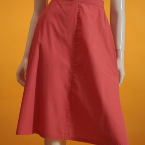 May include: A coral pink A-line skirt with a center seam. The skirt is made of a smooth, lightweight fabric.