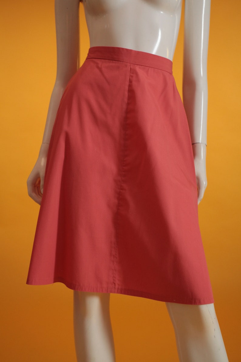 May include: A coral pink A-line skirt with a center seam. The skirt is made of a smooth, lightweight fabric.