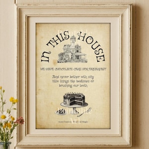 Könnte beinhalten: Gerahmter Vintage-Print mit dem Text „In This House“ und einer skurrilen Hausillustration. Der Druck enthält den Satz „Wir haben Schokoladenkuchen zum Frühstück“. Eine kleine Vase mit Blumen und Bücher befinden sich im Vordergrund.