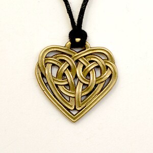May include: A gold-colored heart-shaped pendant with a Celtic knot design. The pendant is hanging from a black cord.