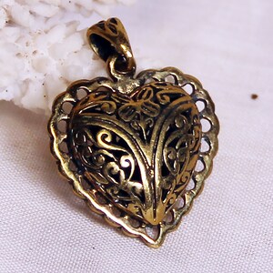 May include: A gold-toned heart-shaped pendant with intricate filigree details. The pendant has a delicate, openwork design and a loop at the top for attaching a chain.