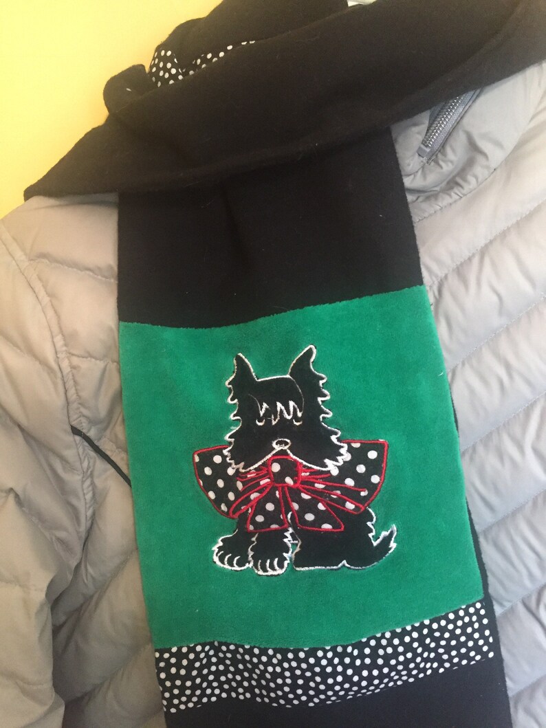 May include: Black scarf with a green panel featuring a black dog with a red and white polka dot bow. The scarf has a black and white polka dot border and is made of a soft material.