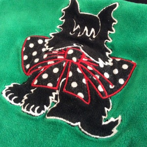 May include: A green textile with a black dog applique. The dog has a white and black polka dot bow with a red outline. The dog's silhouette is black with white accents.