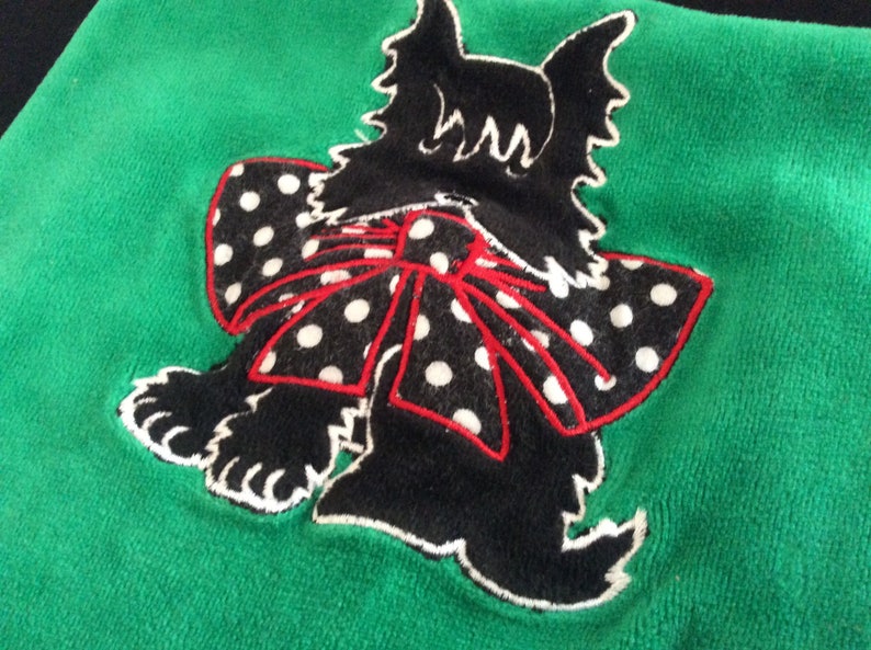 May include: A green textile with a black dog applique. The dog has a white and black polka dot bow with a red outline. The dog's silhouette is black with white accents.