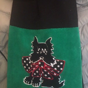 May include: A black and green scarf featuring an embroidered black Scottish Terrier dog with a white polka dot bow and red trim. The top portion of the scarf is black.