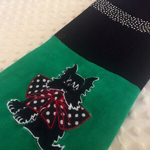 May include: A black and green stocking with a cat applique. The cat is black with a white outline and a red and white polka dot bow. The top of the stocking is black with a white polka dot stripe.