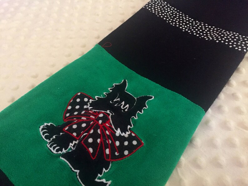 May include: A black and green stocking with a cat applique. The cat is black with a white outline and a red and white polka dot bow. The top of the stocking is black with a white polka dot stripe.