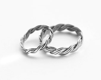 May include: Two silver braided rings, intertwined together. The rings are made of a thick, twisted metal and have a smooth, polished finish.