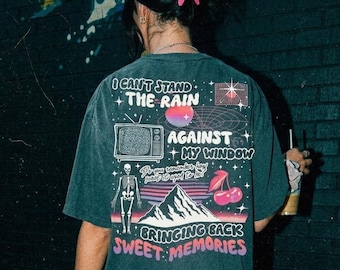 Può includere: Una t-shirt a maniche corte grigio antracite scuro con una stampa grafica sul retro che riporta il testo I CAN'T STAND THE RAIN AGAINST MY WINDOW, Do you remember how sweet it used to be, e BRINGING BACK SWEET MEMORIES, con uno scheletro, un televisore, una montagna e ciliegie.
