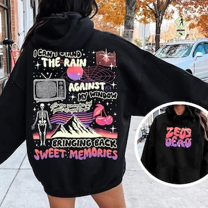 May include: Black hooded sweatshirt with a graphic print on the back. The print features a retro-style design with a TV, a mountain, cherries, and the text "I can't stand the rain against my window, bringing back sweet memories".
