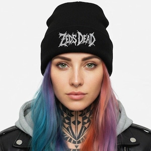 May include: Black beanie with the text "Zeds Dead" in white, stylized lettering. The beanie is worn by a person with multi-colored hair and a black leather jacket.