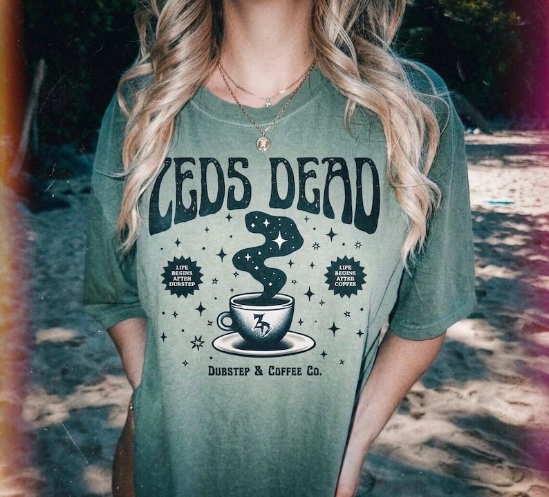May include: Olive green t-shirt with the text "CEDS DEAD" in a retro font. Below the text is a graphic of a coffee cup with a swirling design and the text "Dubstep & Coffee Co."