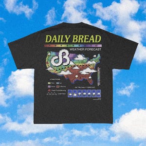 Può includere: Una t-shirt grigio antracite con una stampa grafica di una mappa meteorologica degli Stati Uniti. Il testo recita DAILY BREAD e WEATHER FORECAST. La mappa include una legenda per condizioni come pioggia, neve, ghiaccio e temporali.