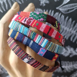 以下が含まれることがあります： さまざまなパターンを持つ、カラフルな織りブレスレットのセット。ブレスレットは、赤、青、緑、黄、黒など、さまざまな色で作られています。