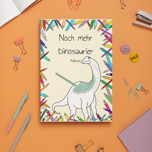 May include: A colouring book with a colourful dinosaur on the cover. The cover is surrounded by colourful pencils. The title of the book is "Noch mehr Dinosaurier Malbuch".