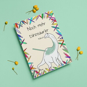 May include: A colouring book cover with a colourful border of pencils surrounding a black and white illustration of a dinosaur. The title of the book is "Noch mehr Dinosaurier" with the word "Malbuch" underneath.