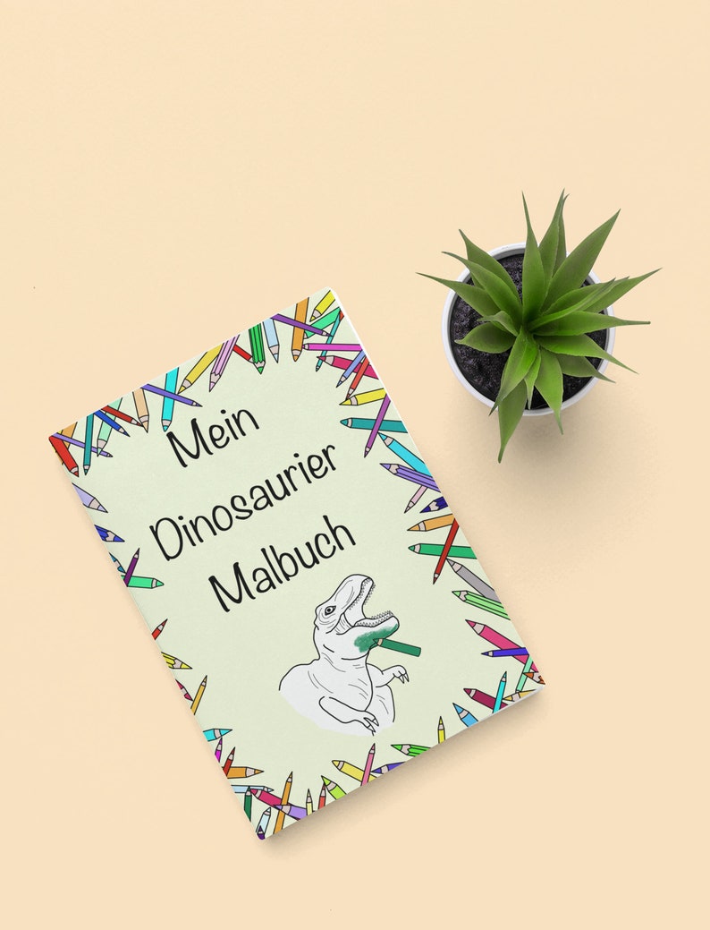 May include: A coloring book titled "Mein Dinosaurier Malbuch" with a dinosaur illustration, surrounded by a border of colorful pencils. A small potted succulent sits beside the book on a light beige surface.