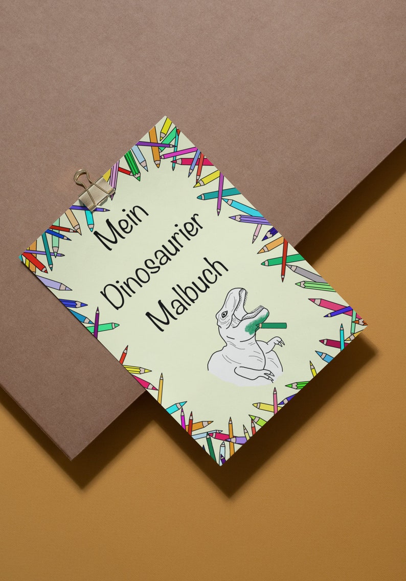 May include: A light green coloring book titled "Mein Dinosaurier Malbuch" with a cartoon dinosaur illustration. The book is surrounded by a border of colorful pencils and held by a silver clip.