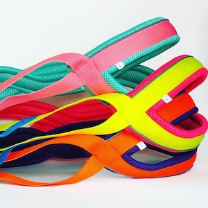 Pode incluir: Uma coleção de bandas de resistência coloridas para exercícios em várias tonalidades, incluindo rosa, verde, amarelo, azul e laranja. Cada banda apresenta um design em laço e uma etiqueta com as letras "NH". As bandas são projetadas para fitness e exercício.