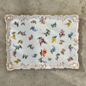May include: A rectangular white porcelain serving tray featuring a hand-painted scattered floral pattern in various colors including pink, blue, yellow, and orange. The tray has a raised, scalloped edge with gold-painted trim details.