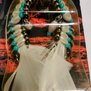 May include: A white feather air freshener with turquoise and white beads, black beads, and silver accents. The air freshener is packaged in a clear plastic bag with a red and black background.