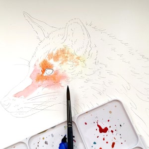 May include: Watercolor painting in progress of a fox's head, featuring orange, peach, and white hues. The fox is sketched in pencil, with watercolor applied to the face. A paintbrush and paint palette with colorful splatters are in the foreground.