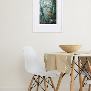 May include: A framed art print depicts a forest scene with a fox, owl, and moon. The artwork is in a white frame and hangs on a white wall. A white chair and table with a wooden bowl and beige tablecloth are in the foreground.
