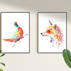 May include: Two framed watercolor prints. One features a colorful pheasant with red, orange, green, and blue hues. The other depicts a fox head in shades of orange, pink, and purple. Both are on white backgrounds.