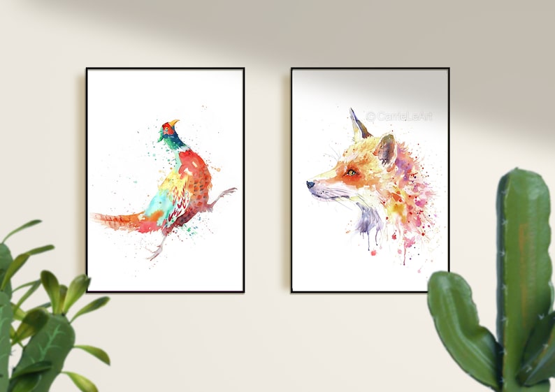 May include: Two framed watercolor prints. One features a colorful pheasant with red, orange, green, and blue hues. The other depicts a fox head in shades of orange, pink, and purple. Both are on white backgrounds.