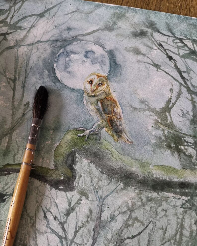 May include: Watercolor painting of a barn owl perched on a mossy branch, set against a backdrop of a full moon and silhouetted trees. The owl has brown and white feathers. A paintbrush is in the foreground.