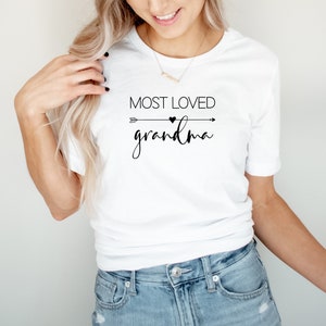 May include: White t-shirt with black text that reads "Most Loved Grandma" with an arrow and heart graphic.