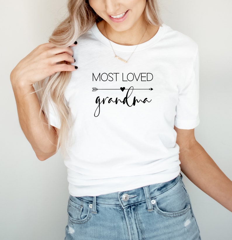 May include: White t-shirt with black text that reads "Most Loved Grandma" with an arrow and heart graphic.