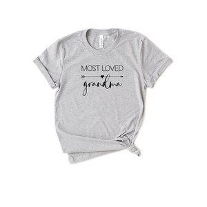 May include: Gray t-shirt with black text that reads "Most Loved Grandma" with an arrow and heart graphic.