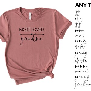May include: A mauve t-shirt with the text "MOST LOVED grandma" in black lettering with an arrow and heart graphic. The text "ANY TEXT" is listed on the right side of the image with a list of different names for grandmother in black lettering.
