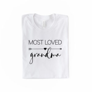 May include: White t-shirt with black text that reads "Most Loved Grandma" with an arrow and heart graphic.