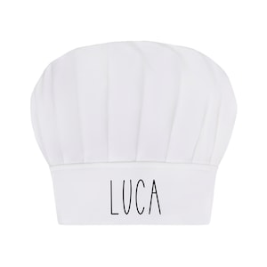 May include: White chef's hat with the name "LUCA" written in black on the front.
