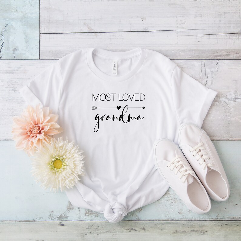 May include: White t-shirt with black text that reads "Most Loved Grandma" with an arrow and heart graphic.