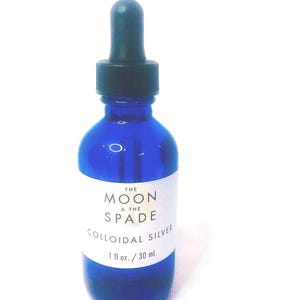 May include: A blue glass bottle with a dropper top, labeled "The Moon & The Spade Colloidal Silver 1 fl oz. / 30 ml."