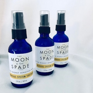 Puede incluir: Tres botellas de spray de vidrio azul con tapas de pulverización negras y etiquetas blancas. Las etiquetas dicen "The Moon & The Spade" y "Para la persona altamente sensible" y "Calmante del sistema nervioso" con una medida de 2 fl oz / 60 ml.