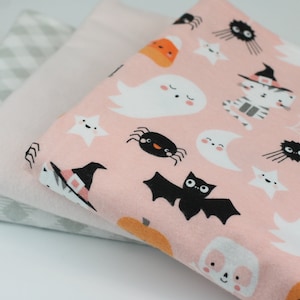 May include: Three fabric pieces: a light pink Halloween-themed print with ghosts, bats, and spiders; a solid light pink; and a gray and white checkered pattern. The Halloween fabric has a variety of cute, cartoonish illustrations.