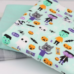 May include: Three fabric pieces: a gray and white checkered pattern, a solid light teal, and a Halloween-themed print. The Halloween fabric features cartoon monsters, pumpkins, bats, and the word "Boo" on a light teal background.
