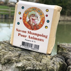 Peut inclure: Un savon brun avec un chien de dessin animé sur l'étiquette. L'étiquette indique "Savon Shampoing Pour Animaux" et "Surgras 6%".